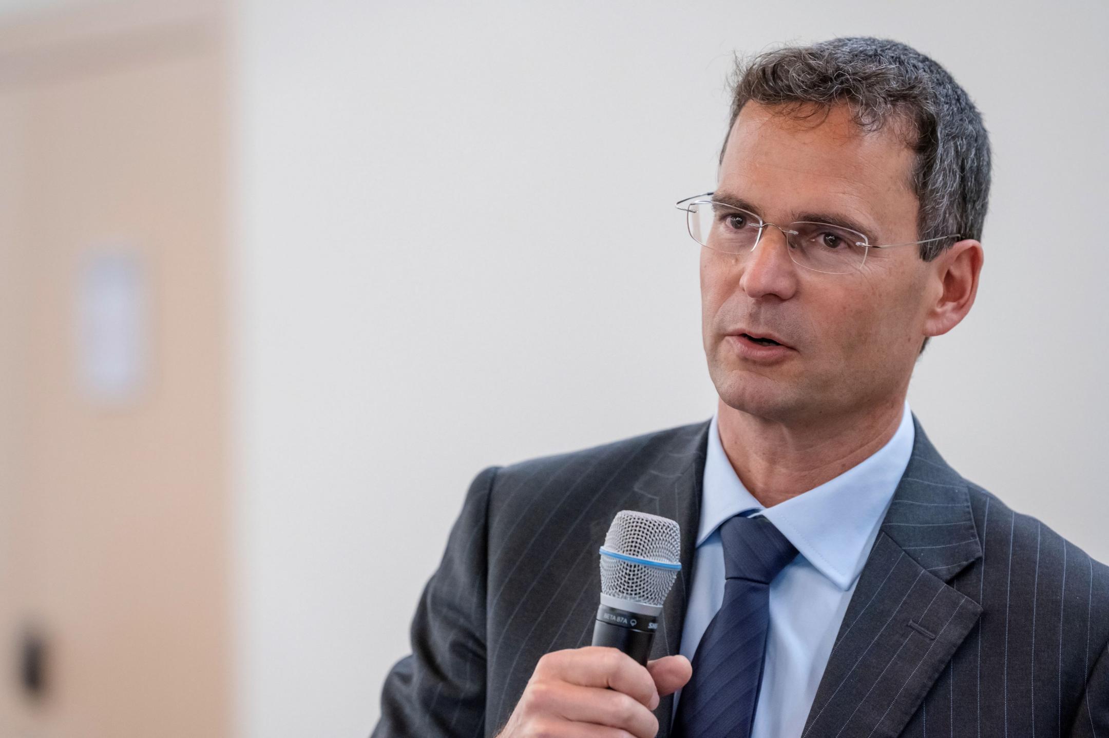 Roger Schuhmacher spricht in ein Mikrophon, das er in seiner rechten Hand hält.