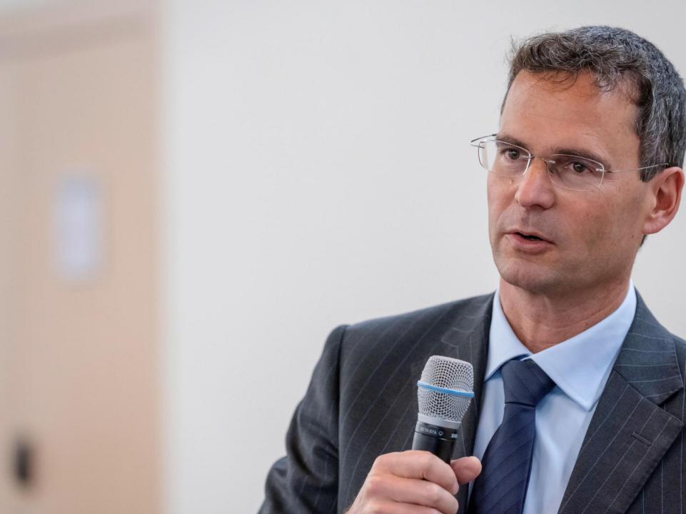 Roger Schuhmacher spricht in ein Mikrophon, das er in seiner rechten Hand hält.