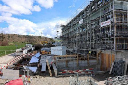 Eine Grossbaustelle. In der Baugrube sieht man die vorderen Umrisse des  fertiggestellten Holzschnitzelbunkers, rechts daneben steht das eingerüstete Schulhaus, das erweitert wird. . 