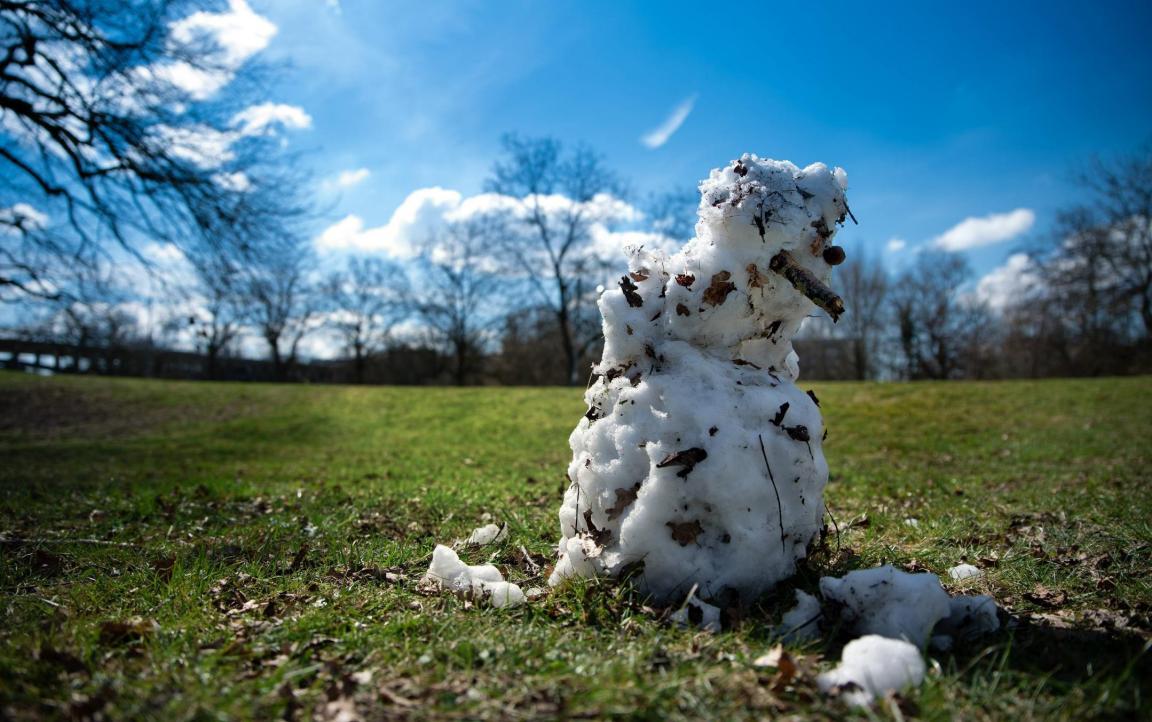 Auf einer grünen Wiese sind die Überreste eines Schneemanns zu sehen, der in der Sonne schmilzt.