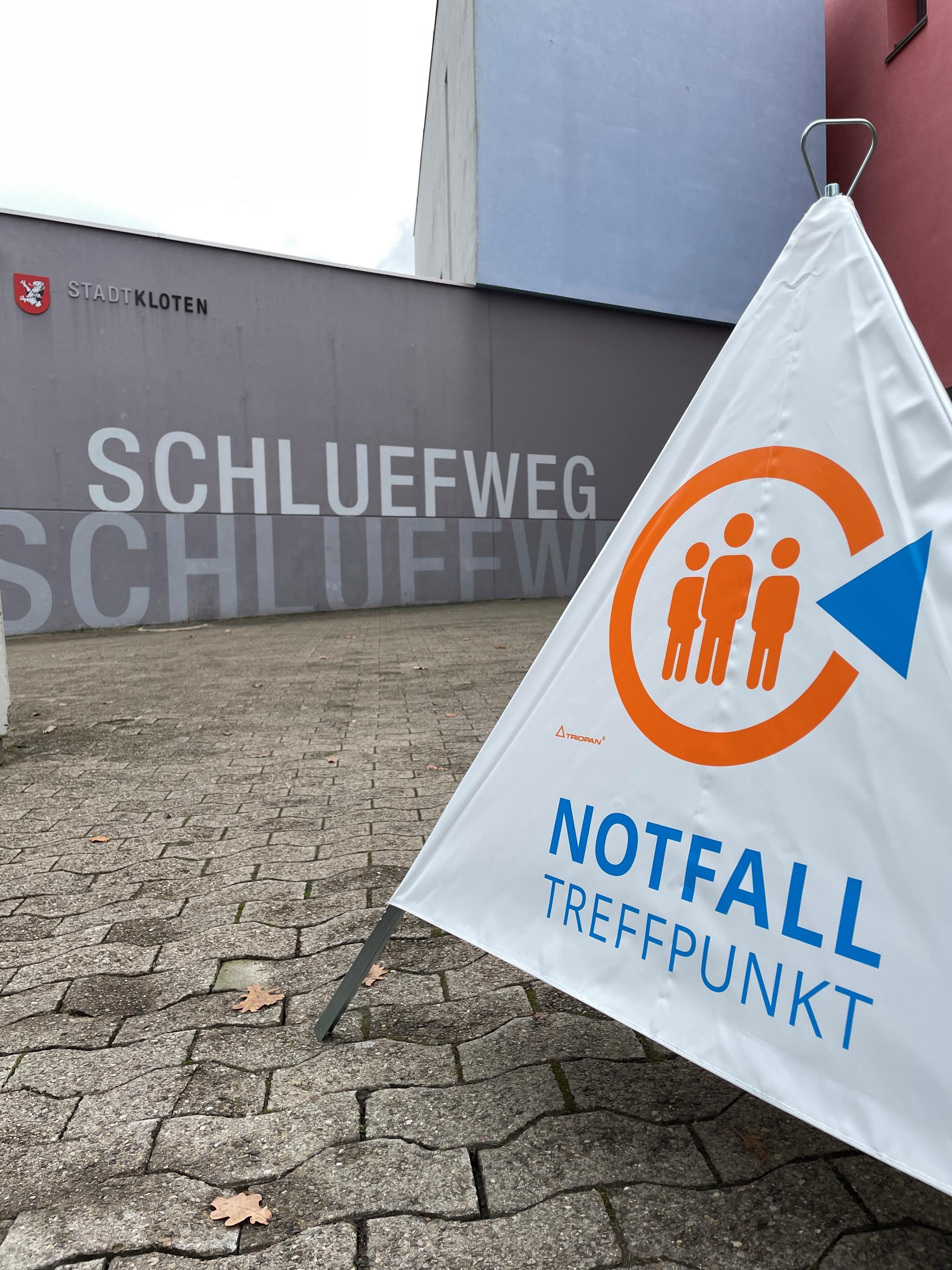 Beim Eingang zum Zentrum Schluefweg, einem modernen Betonbau, steht ein Warndreieck aus weissem Plastik mit der Aufschrift Notfalltreffpunkt. 