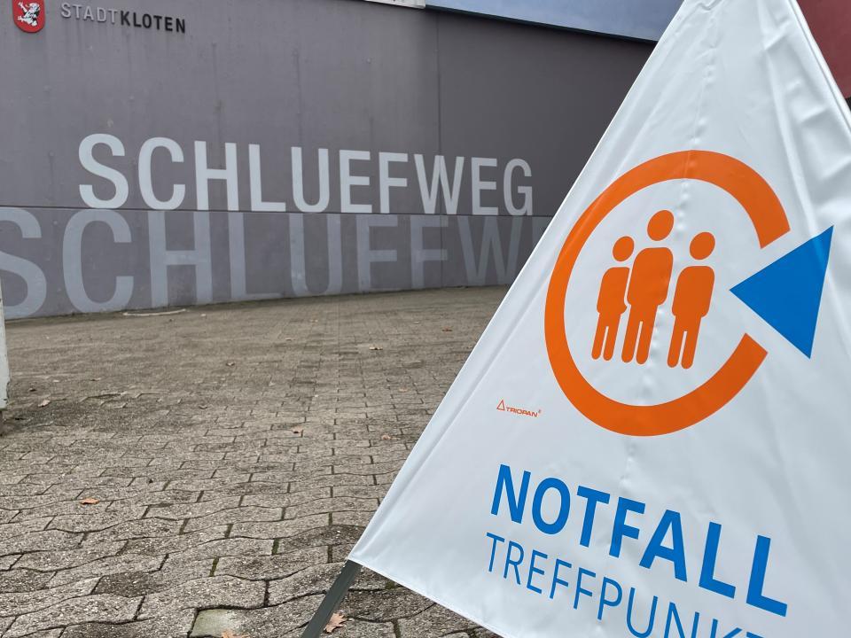 Beim Eingang zum Zentrum Schluefweg, einem modernen Betonbau, steht ein Warndreieck aus weissem Plastik mit der Aufschrift Notfalltreffpunkt. 