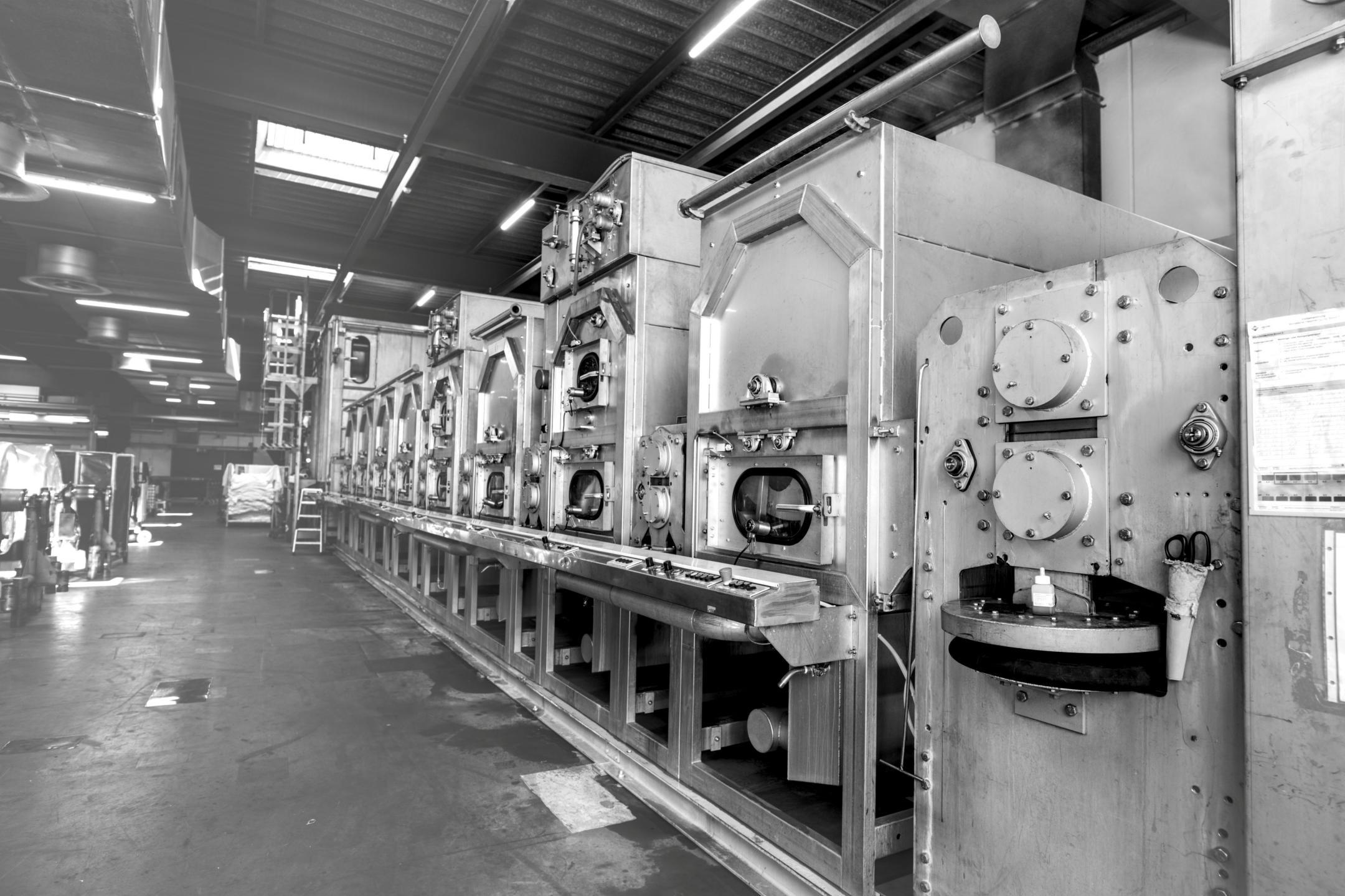 Grosse, dampfbetriebene Textilfixierungsmaschine mit mehreren Kammern und Bedienfeldern in einer Fabrikhalle.