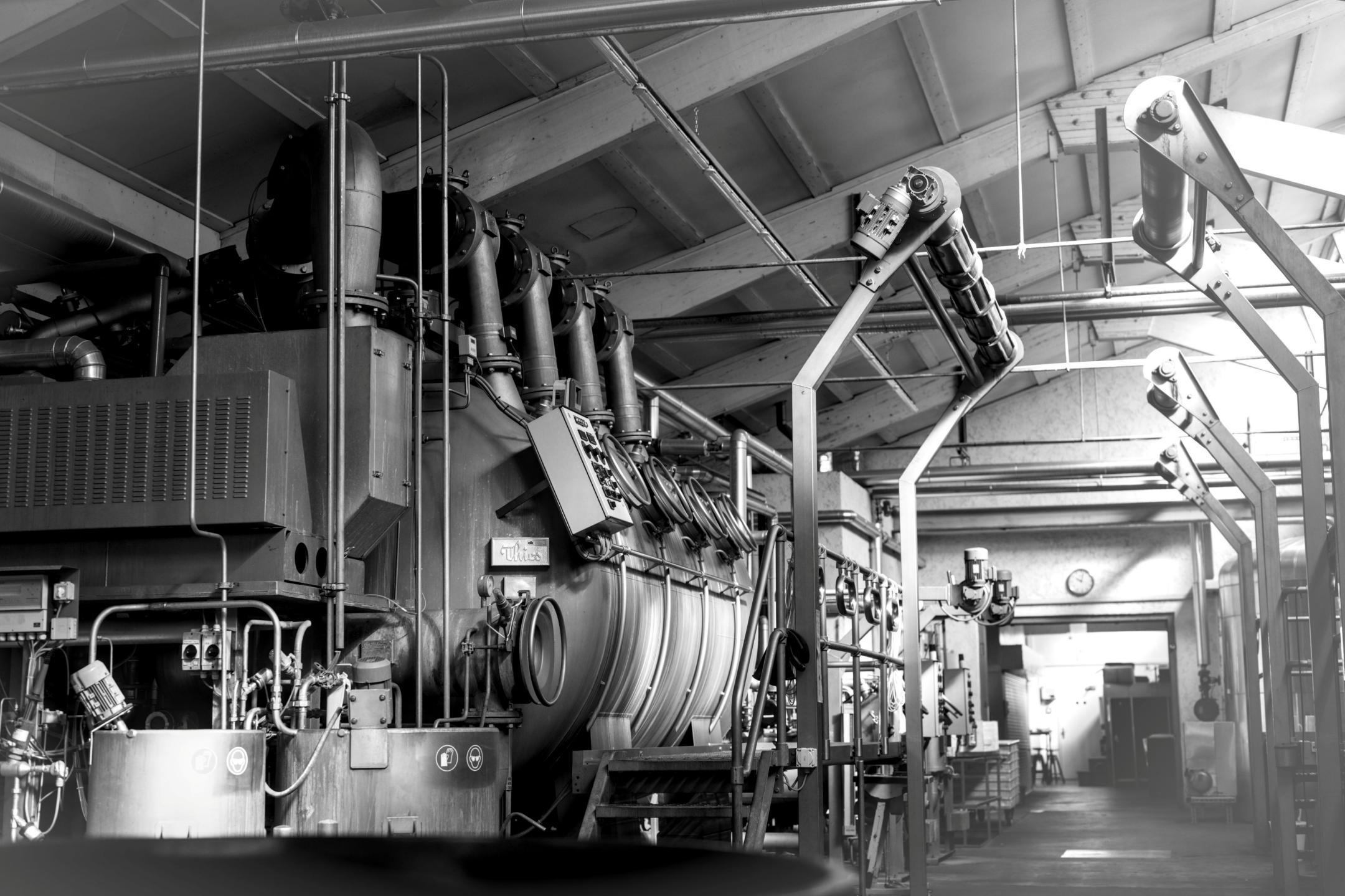 Dampfbetriebene Waschmaschine «Sulzer» mit vielen Rohren und Anschlüssen in einer Fabrikhalle.