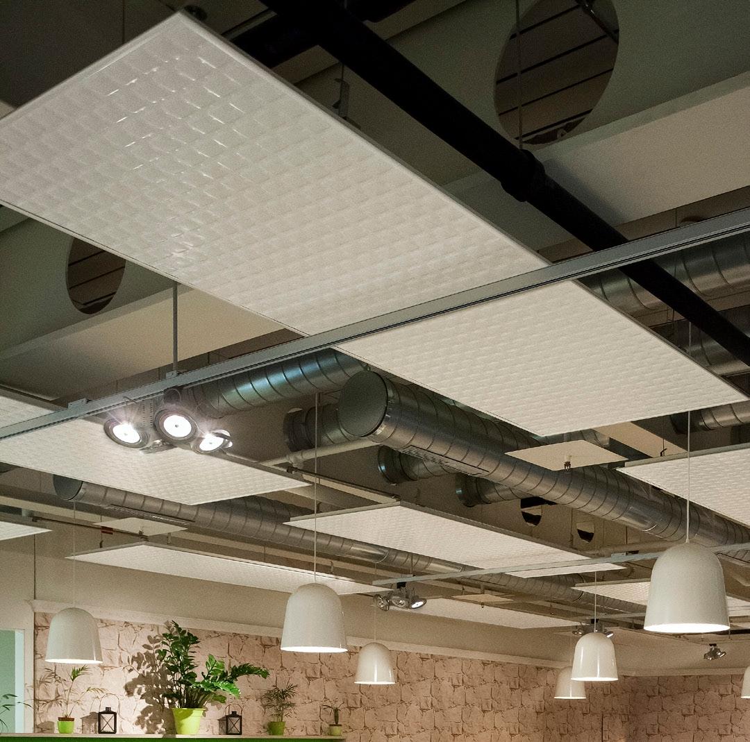 Sichtbare Deckenheizungspaneele mit geriffelter Oberfläche, Lüftungsrohren und Hängelampen in einem Raum mit Backsteinwand.