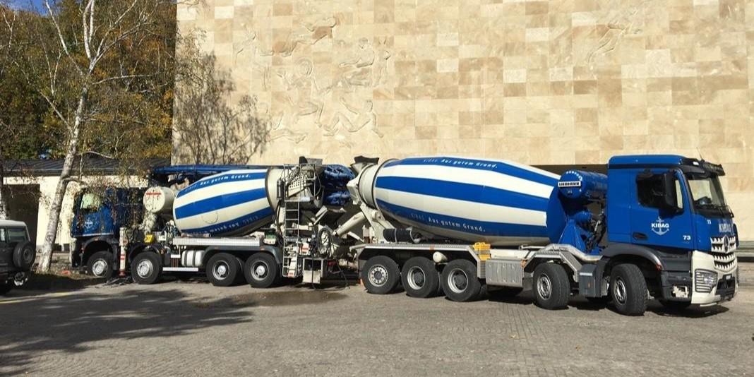  Zwei blaue Betonmischerfahrzeuge stehen nebeneinander vor einer hellen Steinwand im Freien.