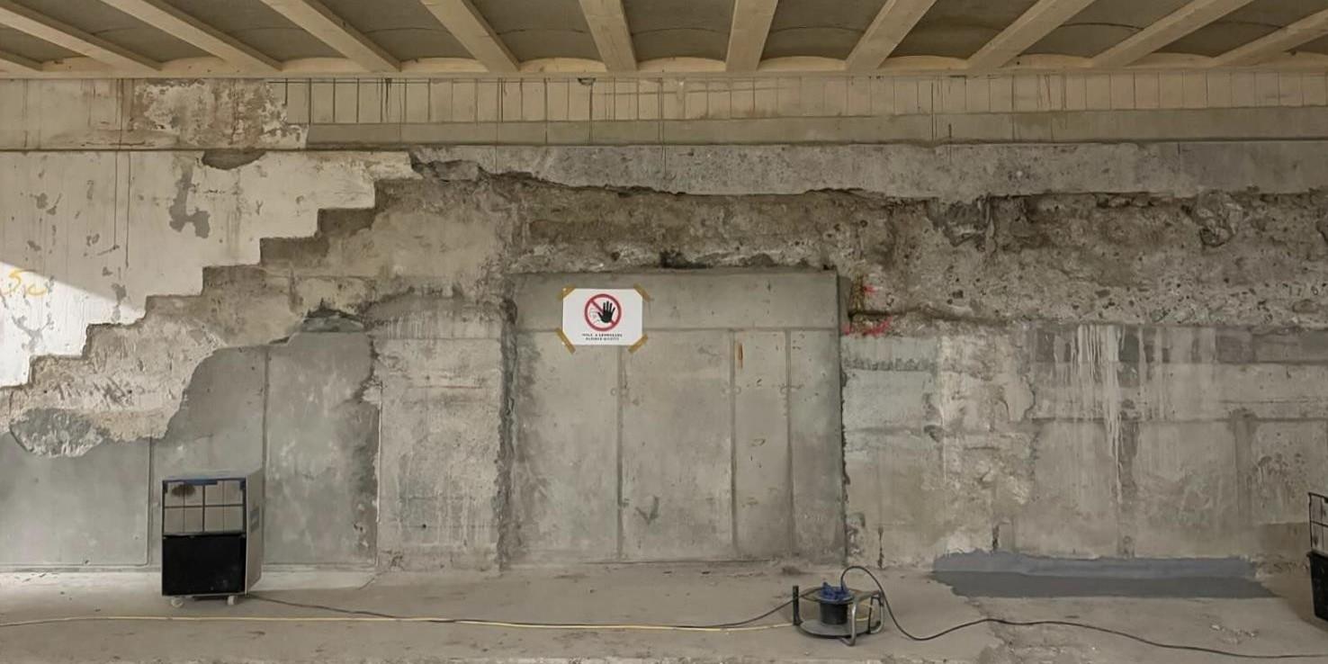 Teilweise freigelegte Betonwand mit sichtbaren Abbruchkanten und einem Warnschild, im Vordergrund ein Messgerät.