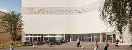 Ansicht des Haupteingangs des Lindt «Home of Chocolate» in Kilchberg mit Terrasse, Sonnenschirmen und Personen im Vordergrund. 