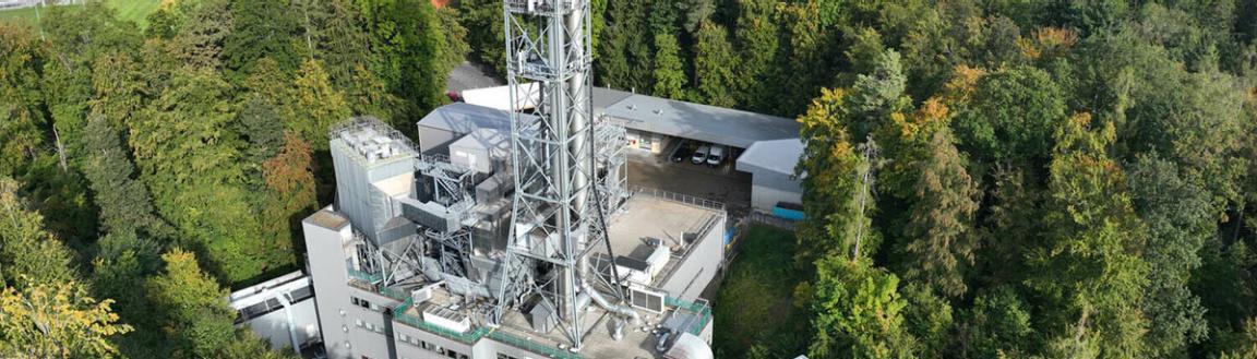 Luftaufnahme einer Kehrichtverwertungsanlage mit hohem Schornstein und technischen Aufbauten, umgeben von Wald und Nebengebäuden. Die Anlage ist Teil eines Projekts zur Produktion von grünem Methanol.