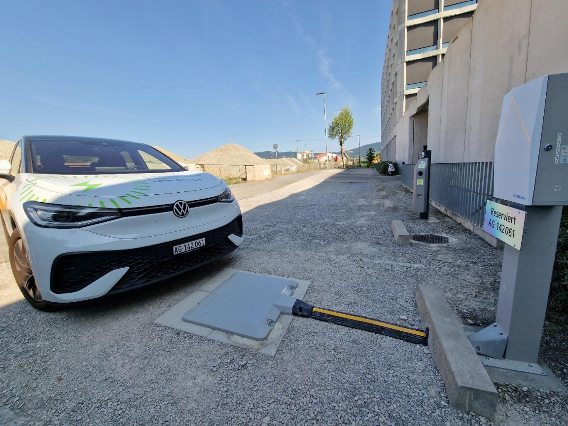 Elektroauto parkiert vor einer induktiven Ladestation mit Bodenpad und Wallbox auf einem Aussenparkplatz.