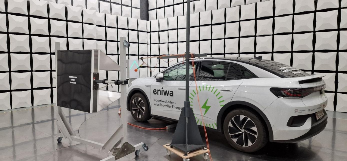 Elektrofahrzeug mit induktivem Ladesystem in einer EMV-Testhalle mit Messgeräten und Antennen.