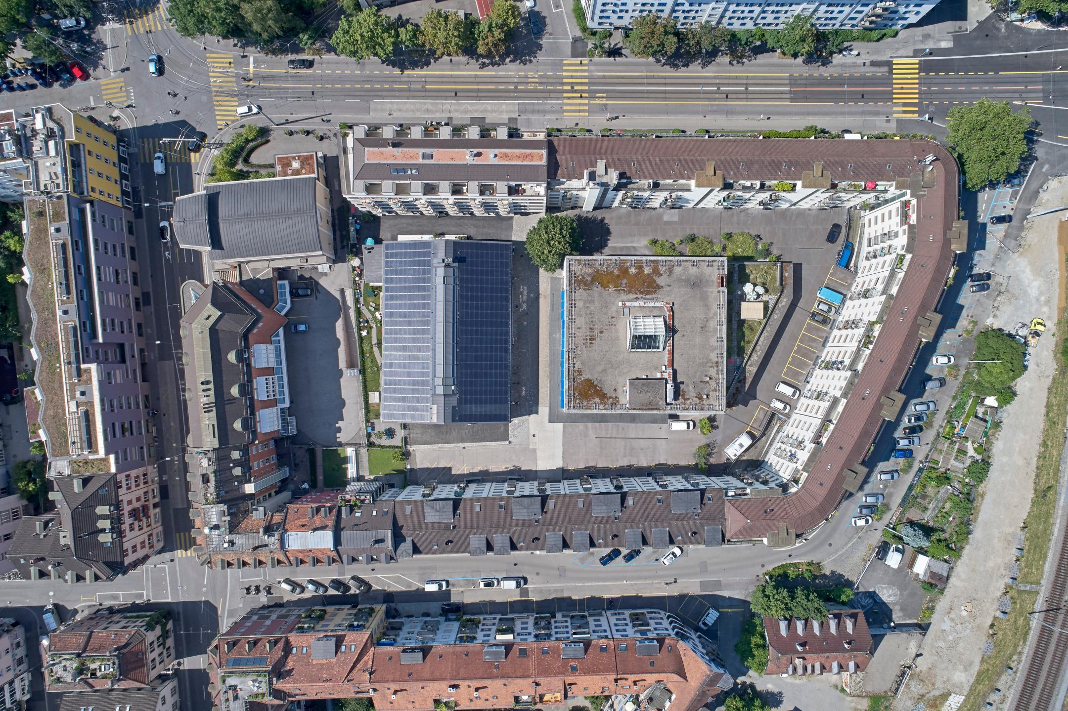 Luftaufnahme senkrecht von oben auf die Liegenschaft Hohlstrasse 100 mit dem geschwungenen Randgebäude entlang der Strasse und dem Hofgebäude mit Photovoltaikanlage im Innenhof.