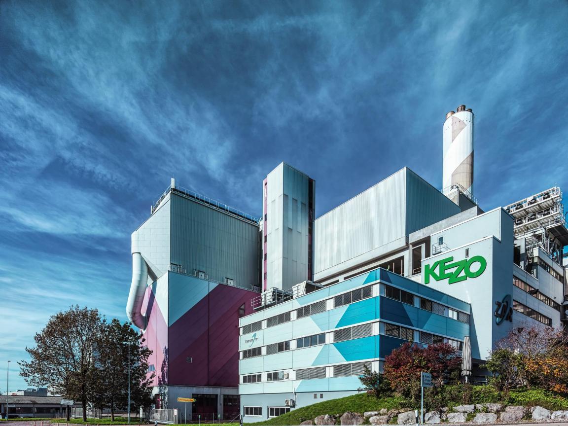 Industriegebäude der KEZO mit markanter Fassade, Schornstein und klarer blauer Himmel im Hintergrund.