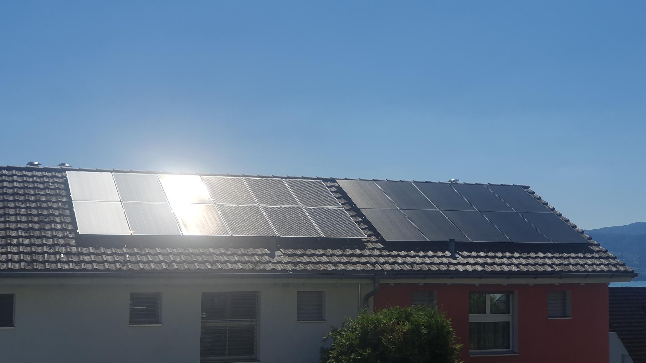 Hausdach mit Photovoltaikmodulen. Die linke Modulreihe zeigt starke Lichtreflexion, die rechte Reihe ist dunkel und blendfrei. Blauer Himmel im Hintergrund.