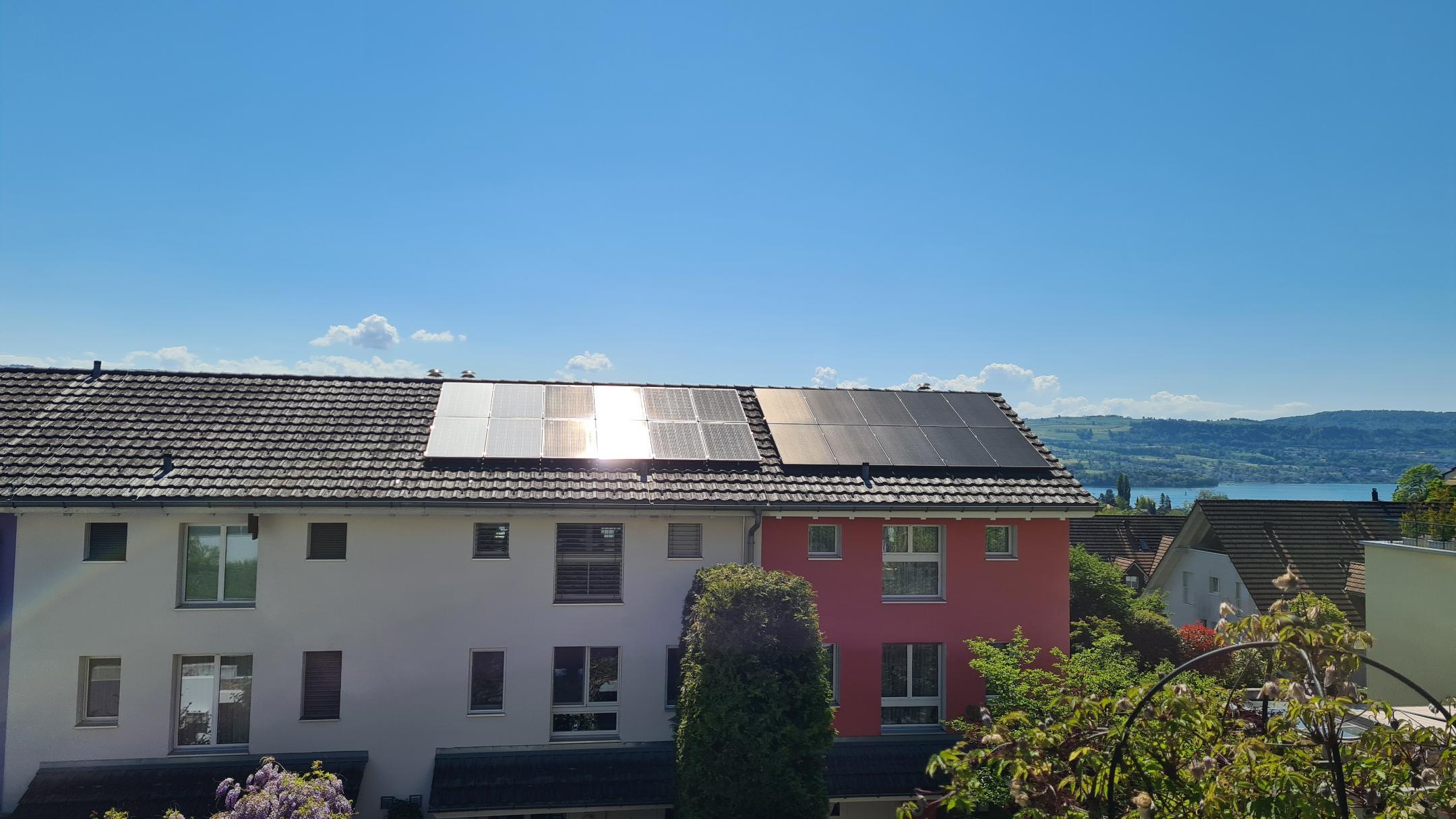 Hausdach mit zwei Reihen Photovoltaikmodulen. Die linke Reihe zeigt deutliche Lichtreflexion, die rechte Reihe ist dunkel und blendfrei. Im Hintergrund blauer Himmel mit Wolken.