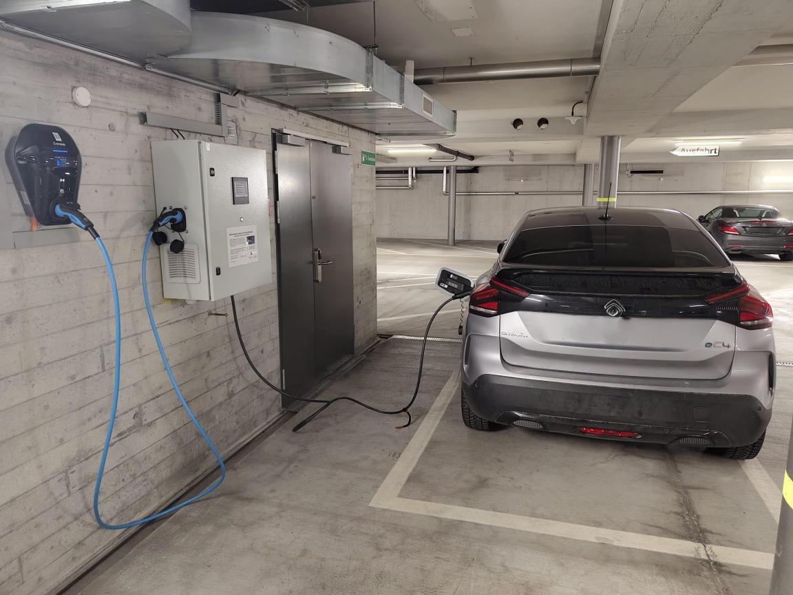 Ein grau-schwarzes Auto wird in einer grauen Tiefgarage geladen.