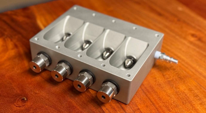 Die Sprühvorrichtung besteht aus zwei Körpern. Der erste Körper aus eloxiertem Aluminium, gefertigt mit 5-Achs-CNC-Bearbeitung, trägt auswechselbare Düsen für Luft und Paste.