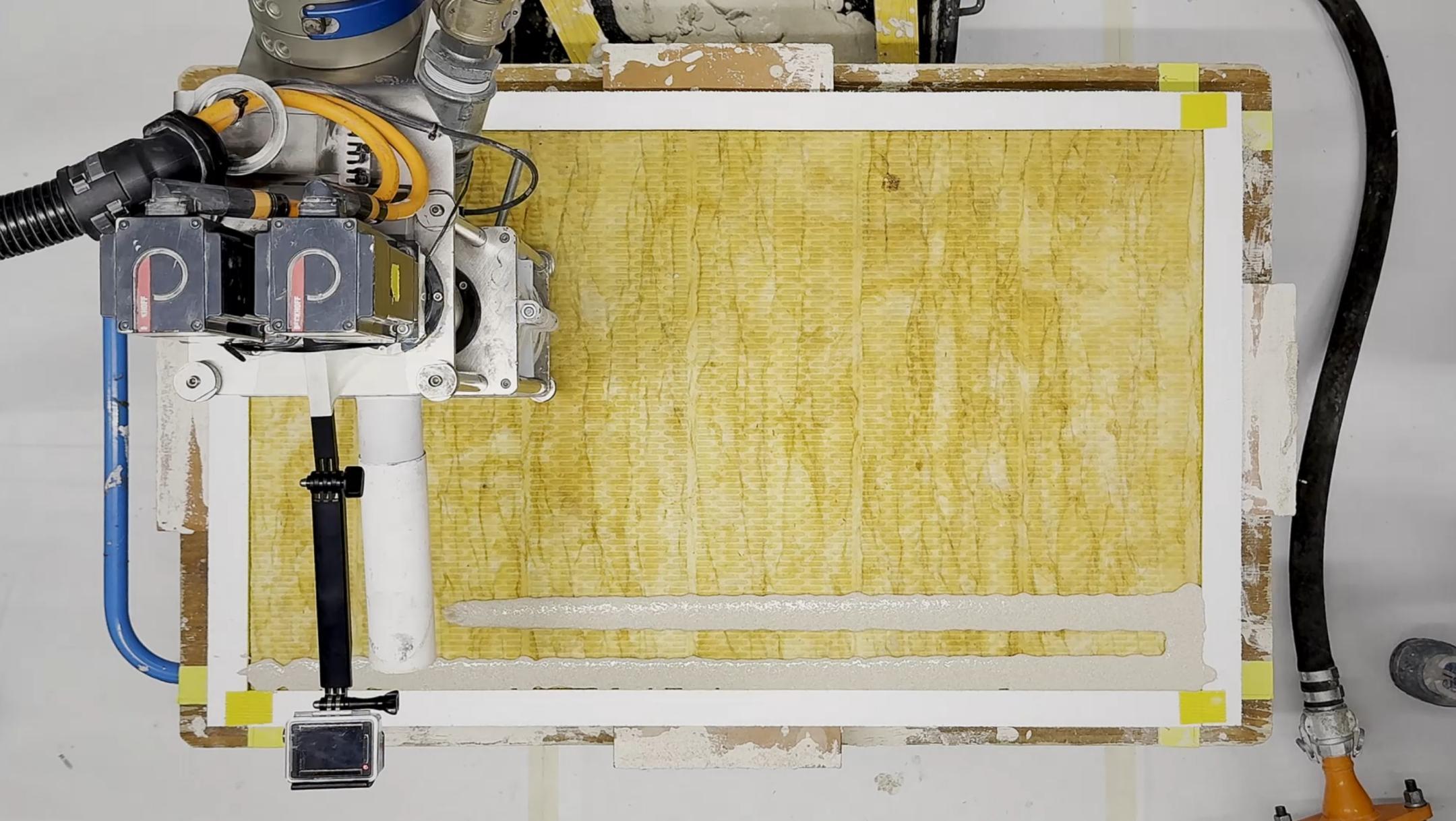 Eine gelbliche Platte liegt unter einem schwebendem Roboterarm.