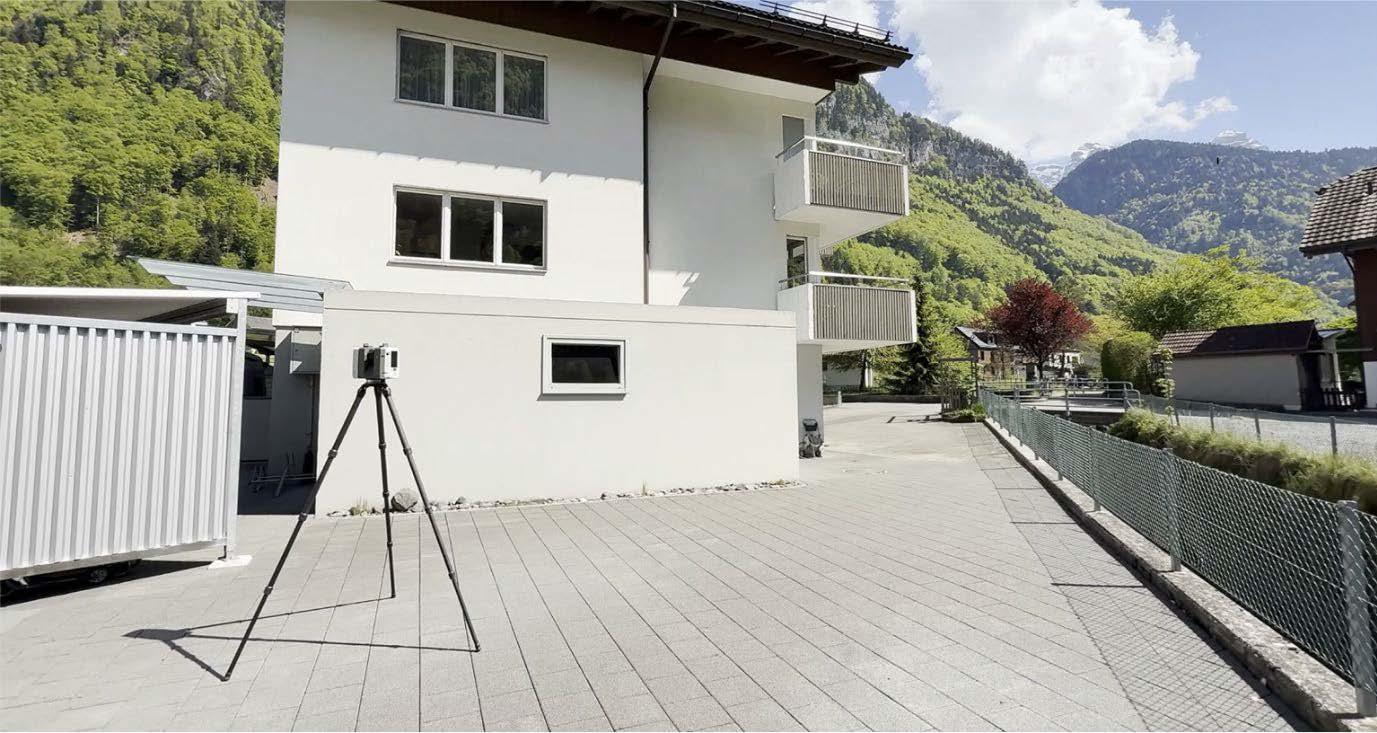 Das Bild zeigt das hochpräzise 3D-Scanning an ausgewählten Standorten rund um das Gebäude. Es wird mit dem Scanner, welcher auf dem Stativ vor dem Gebäude steht eine Aufnahme gemacht.
