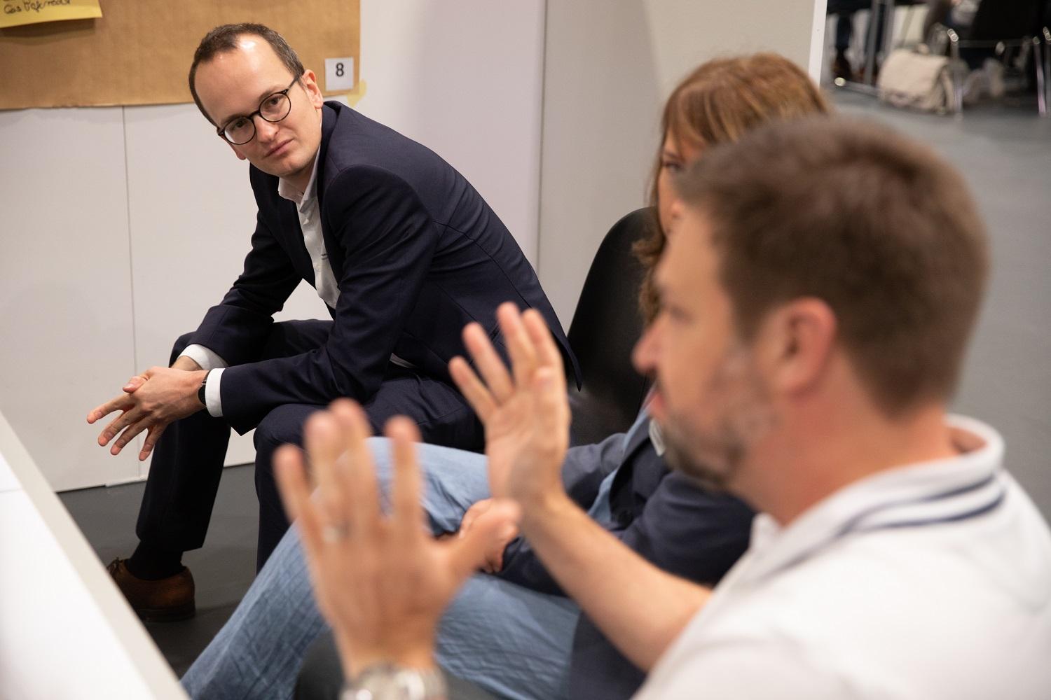 Baudirektor Martin Neukomm sitzt mit einer Workshop-Gruppe am Tisch und hört einem Teilnehmenden zu, der mit grosser Geste argumentiert.