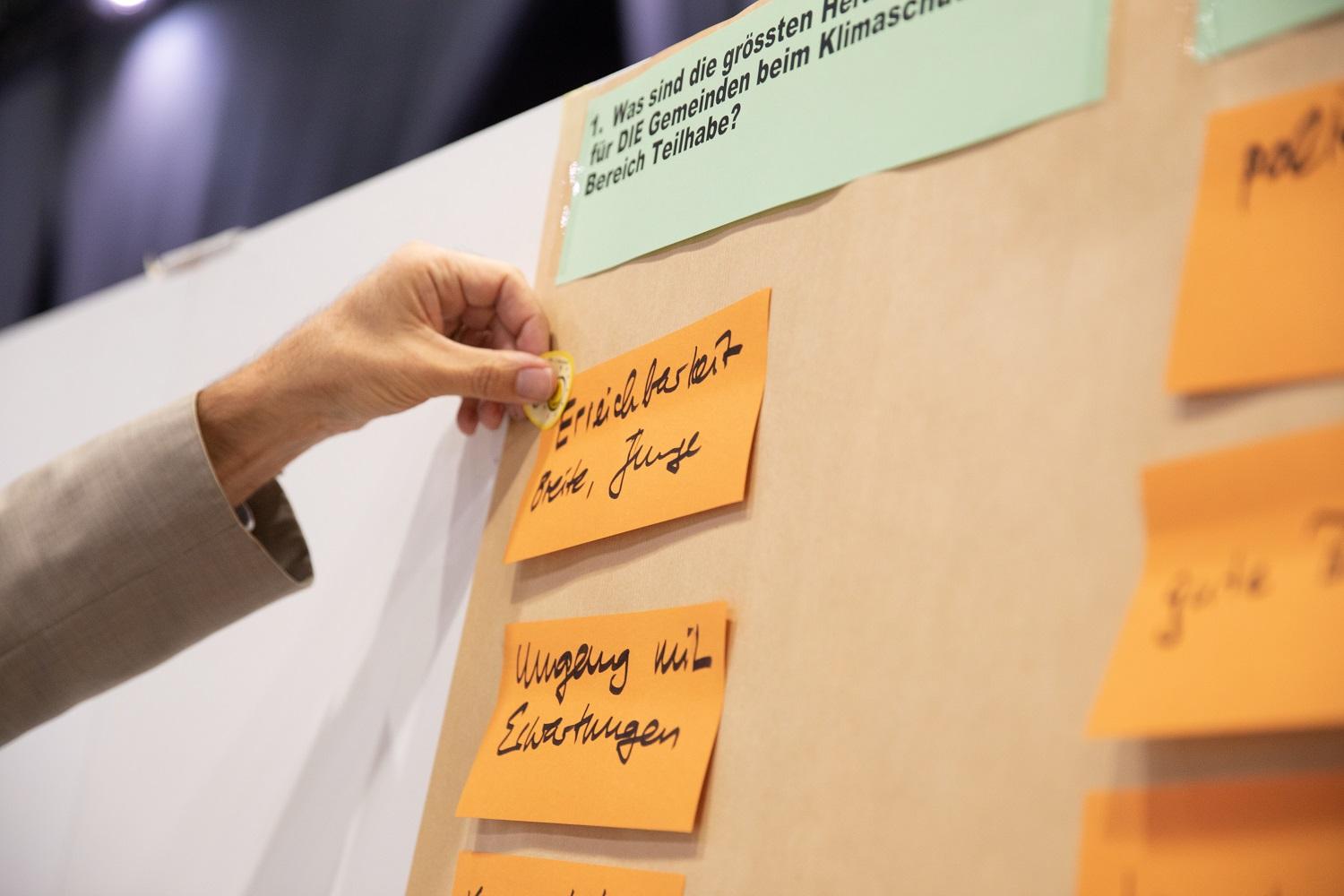 Ein Mitglied einer Workshop-Gruppe am Klimadialog 2021 klebt einen Sticker auf die Ergebnis-Flipchart. 