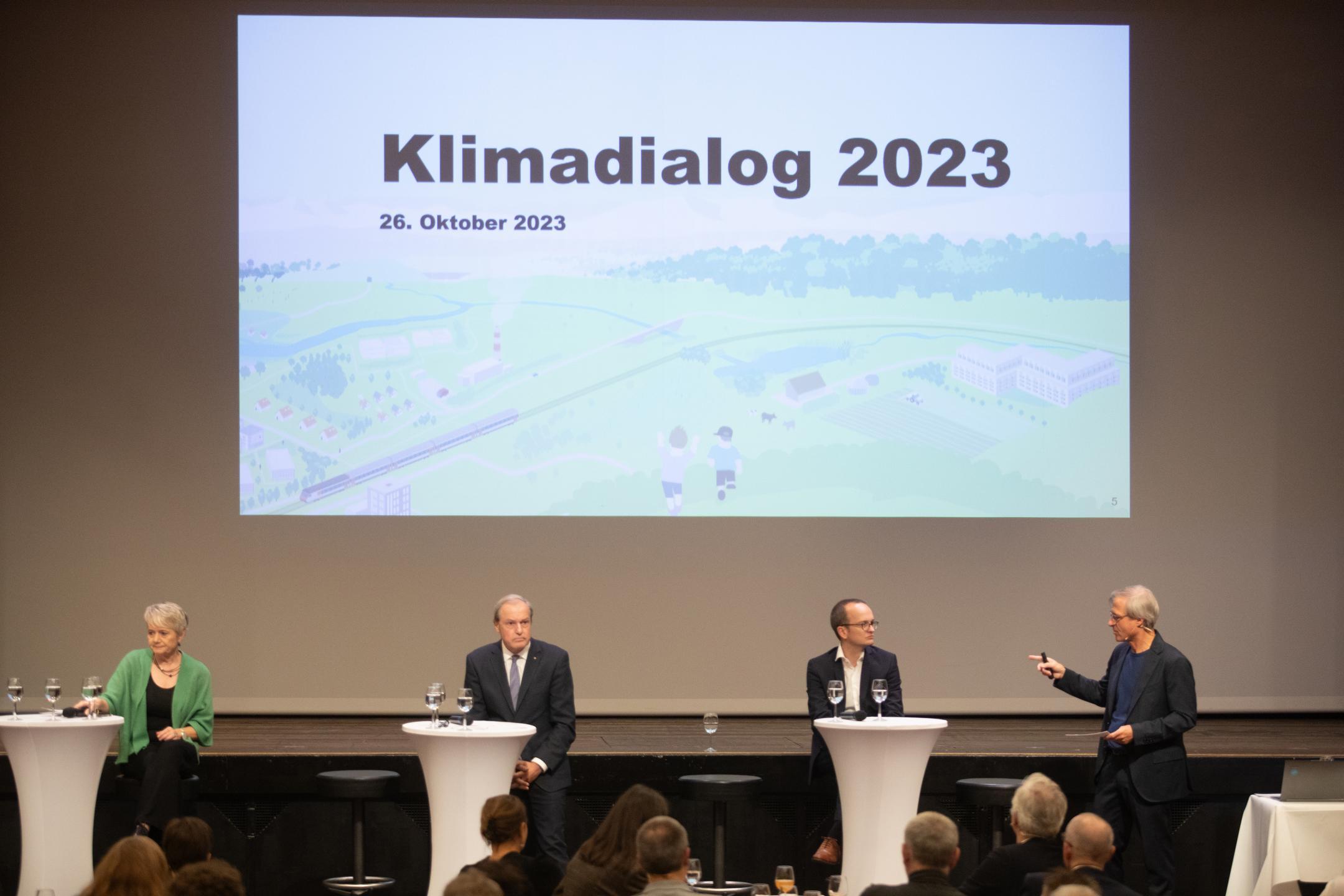 Jacqueline Fehr, Jörg Kündig und Martin Neukom sitzen je an einem Stehtisch auf der Bühne. Rechts von ihnen steht Moderator Michael Emmenegger