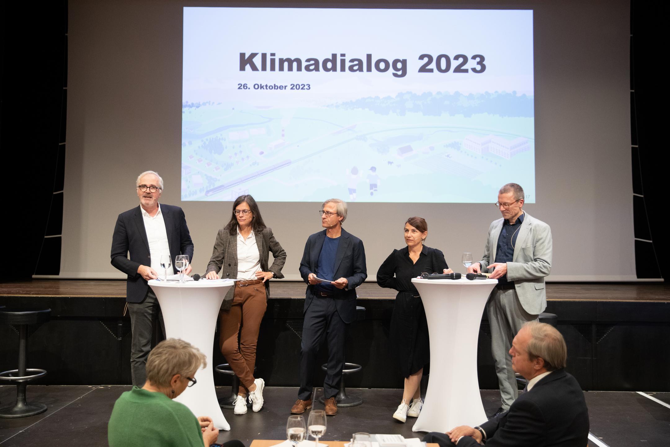 Die Podiumsteilnehmenden stehen nebeneinander auf der Bühne, der Moderator in der Mitte.