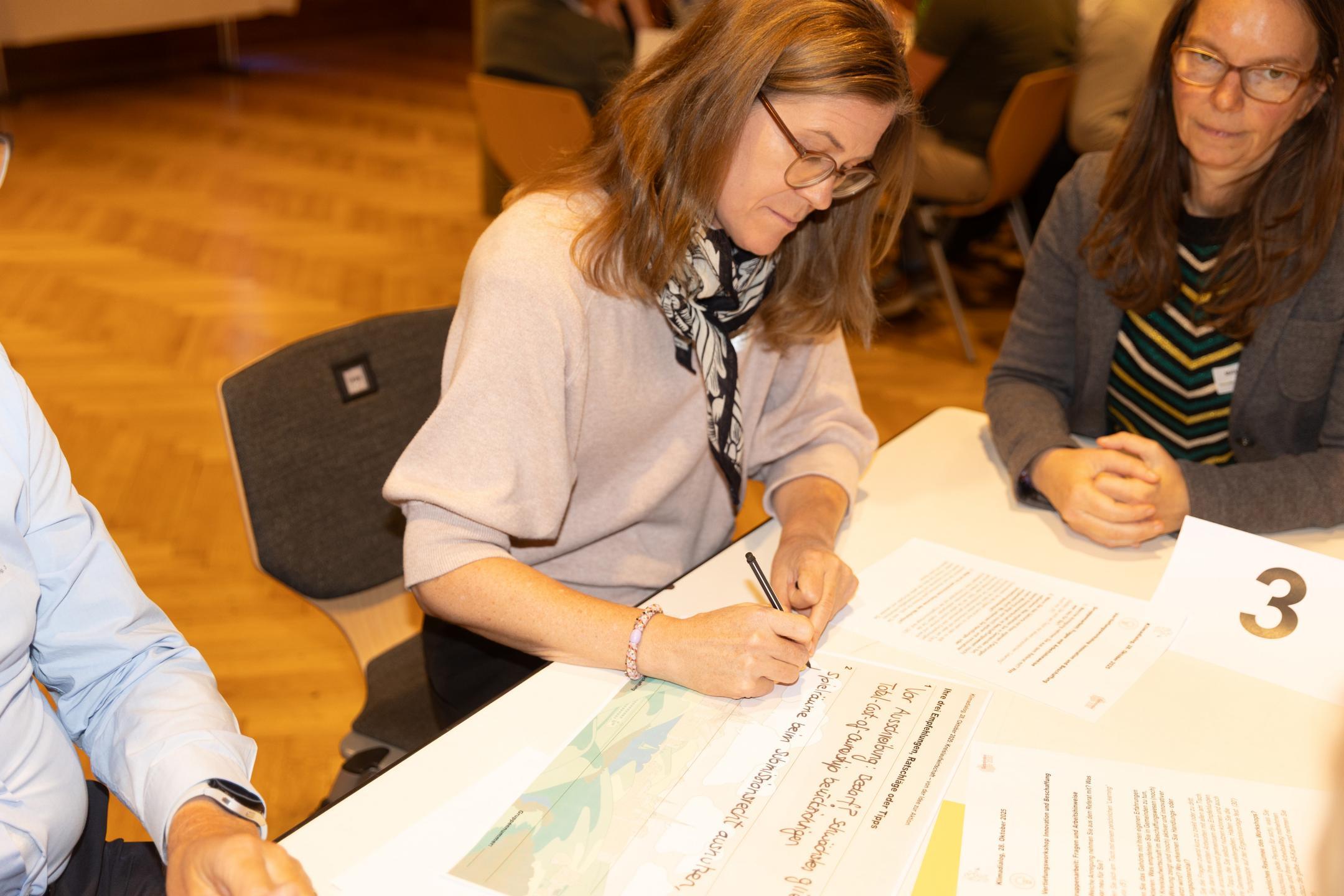 Teilnehmerin eines Workshops schreibt auf ein A3-Blatt