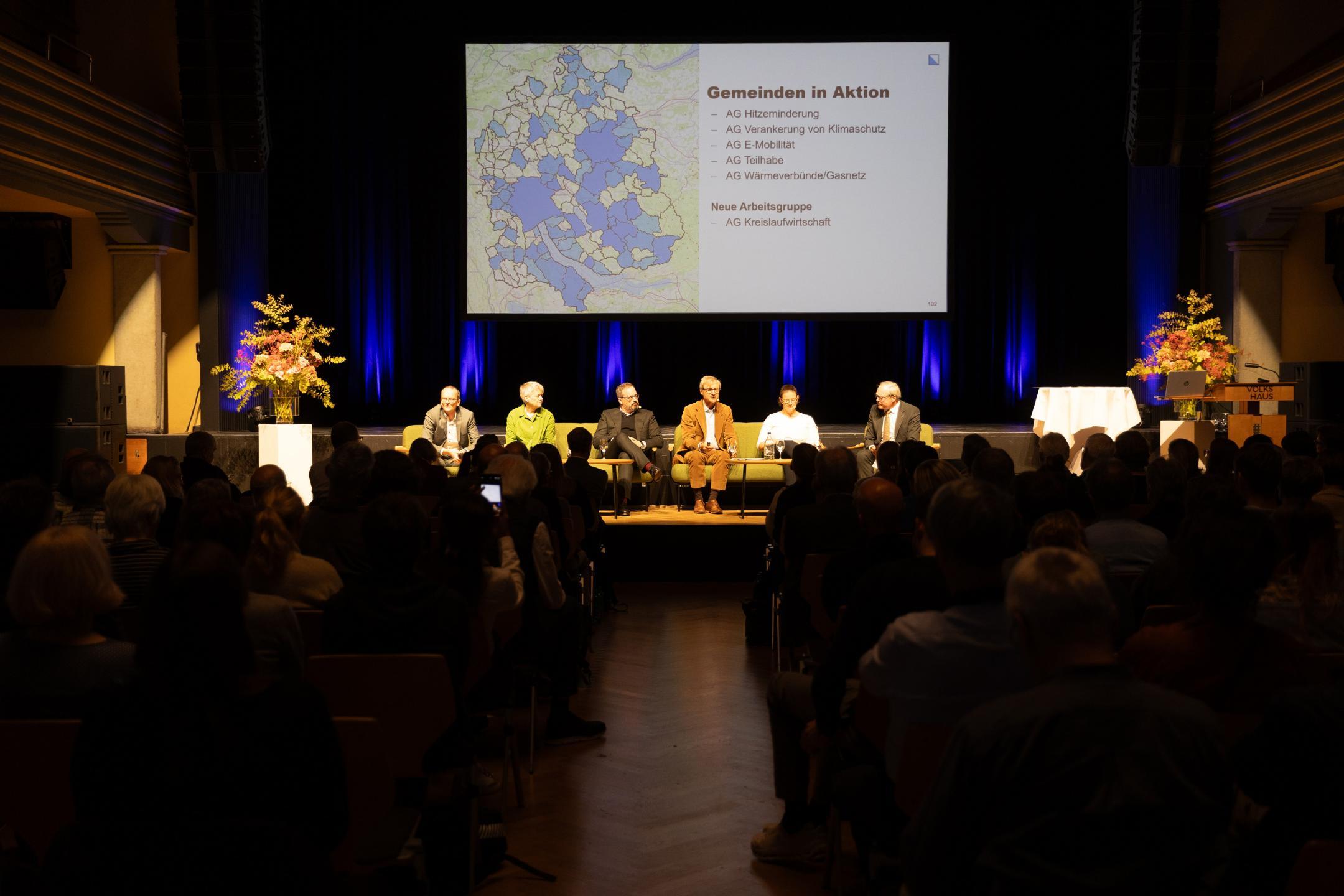 Publikum, Podiumsgäste auf der Bühne, Folie im Hintergrund zeigt, Kantonsumriss, blau eingefärbt sind die Gemeinden, die sich in Arbeitsgruppen engagieren