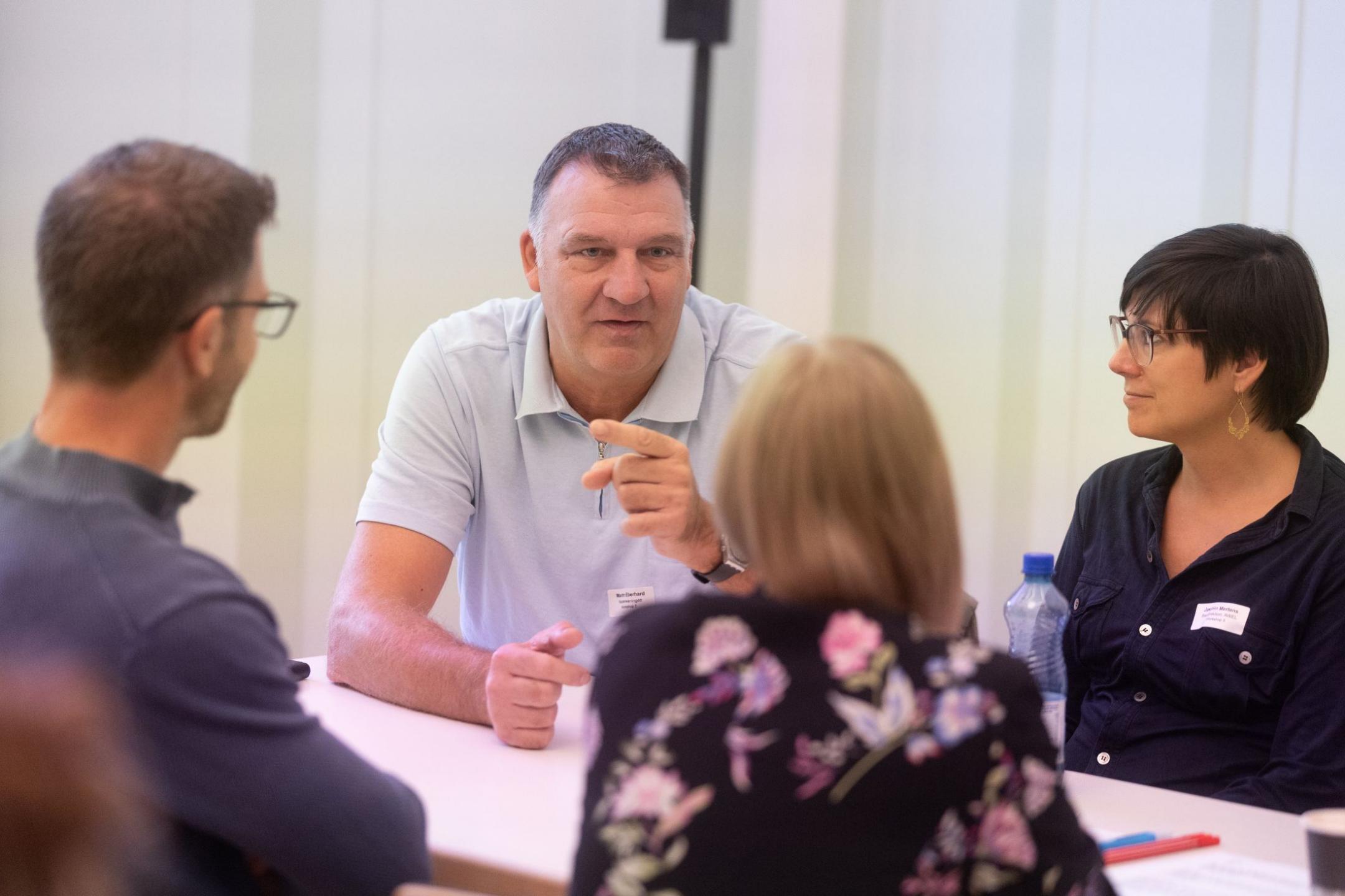 Vier Personen sitzen am Tisch und diskutieren. 