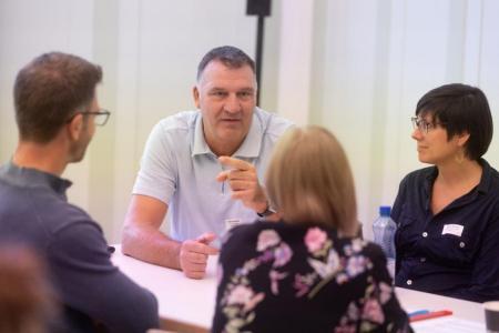 Vier Personen sitzen am Tisch und diskutieren. 