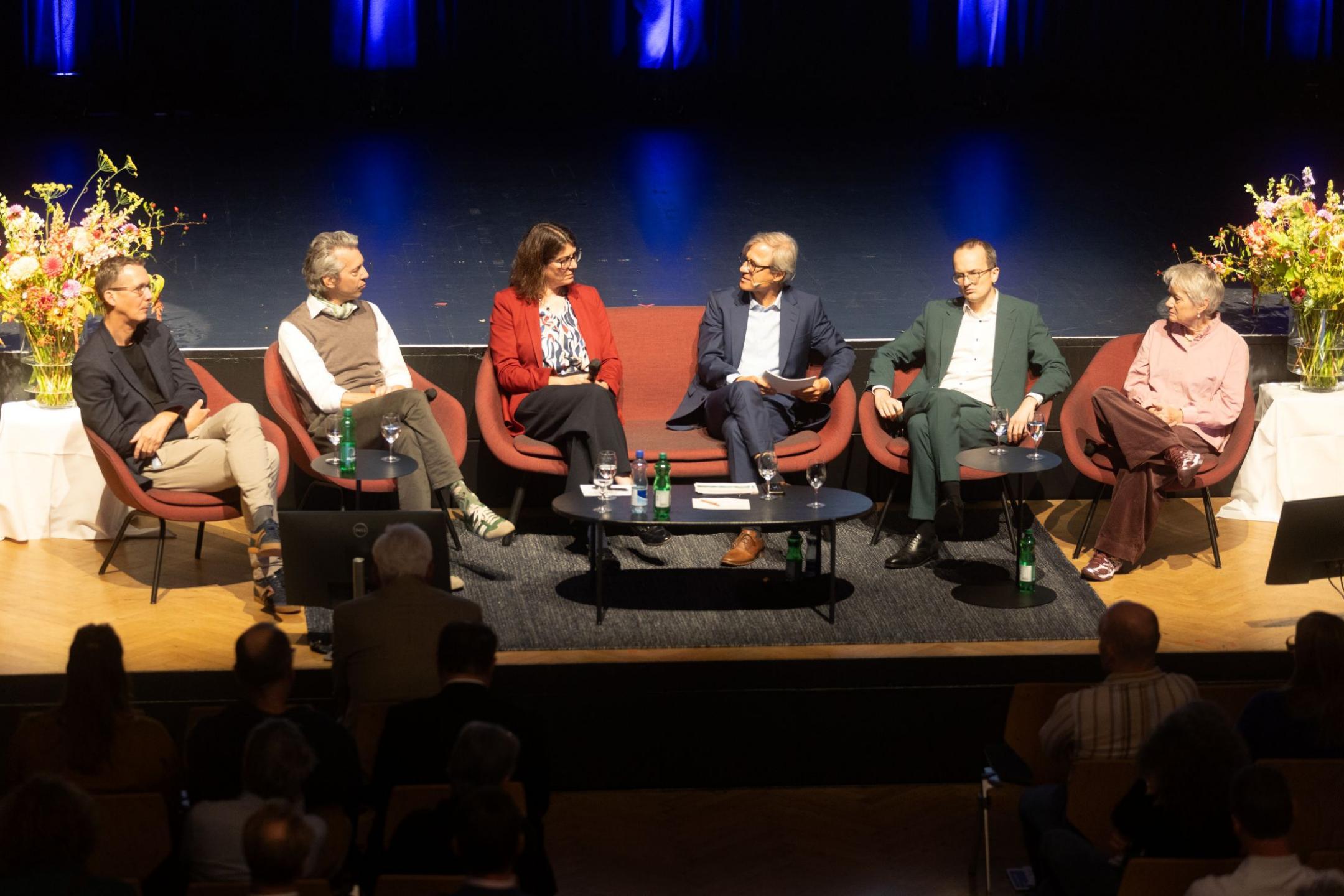 Sechs Personen sitzen für die Podiumsdiskussion auf roten Stühlen auf der Bühne: Michael Hermann (Sotomo), Thomas Ziltener (Co-Präsident VZGV), Monika Keller (Präsidentin GPV), Michael Emmenegger, Moderation, Regierungsrat Martin Neukom und Regierungsrätin Jacqueline Fehr.