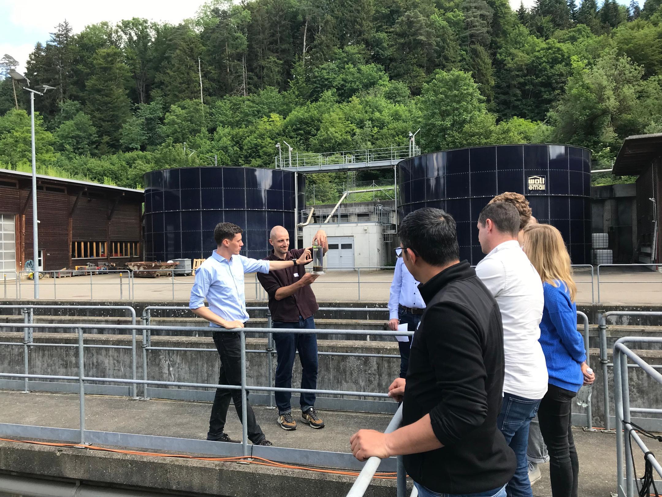 zwei Personen zeigen den Teilnehmenden einen Messbehälter