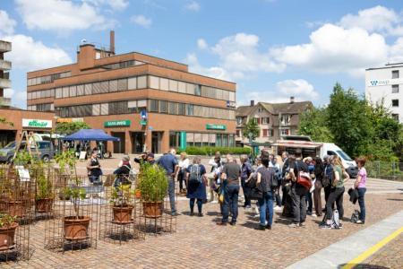 Teilnehmende stehen auf dem gepflasterten Märtplatz zusammen, links eine temporäre Neophyten-Ausstellung, im Hintergrund Backsteingebäude