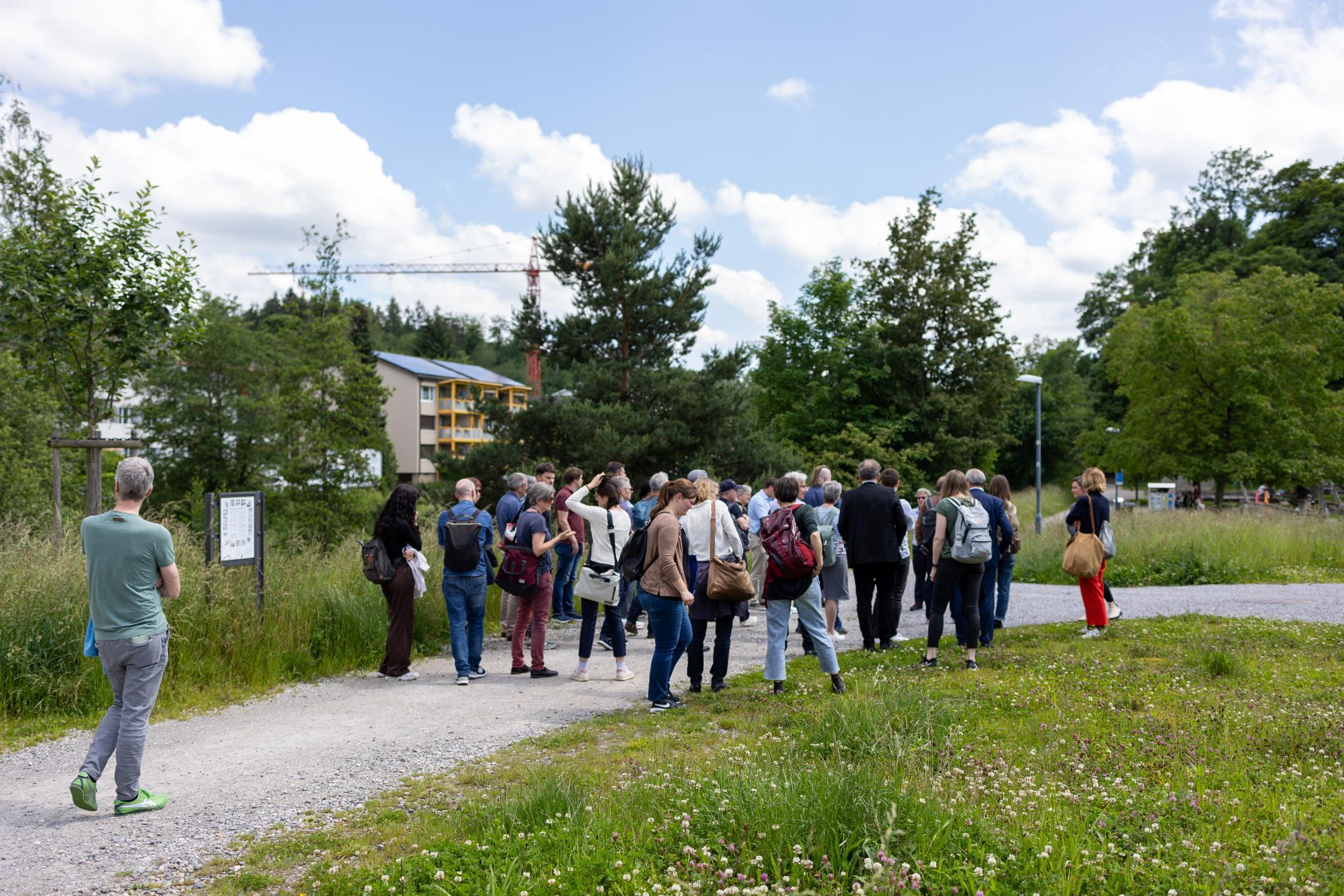 Teilnehmende stehen auf Kiesweg durch das grüne Moosburgareal, im Hintergrund ein Mehrfamilienhaus mit Baukran.