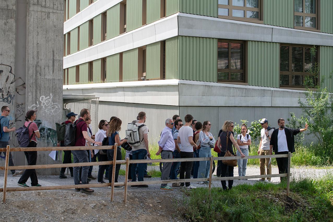 Die Teilnehmenden am Flussufer, im Hintergrund ein Brückenpfeiler und ein Wohnhaus