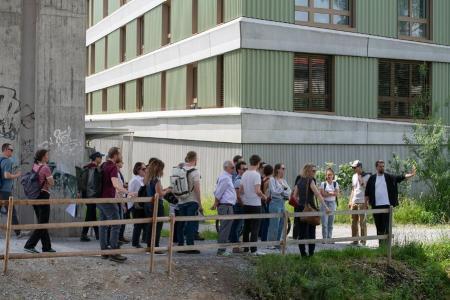 Die Teilnehmenden am Flussufer, im Hintergrund ein Brückenpfeiler und ein Wohnhaus