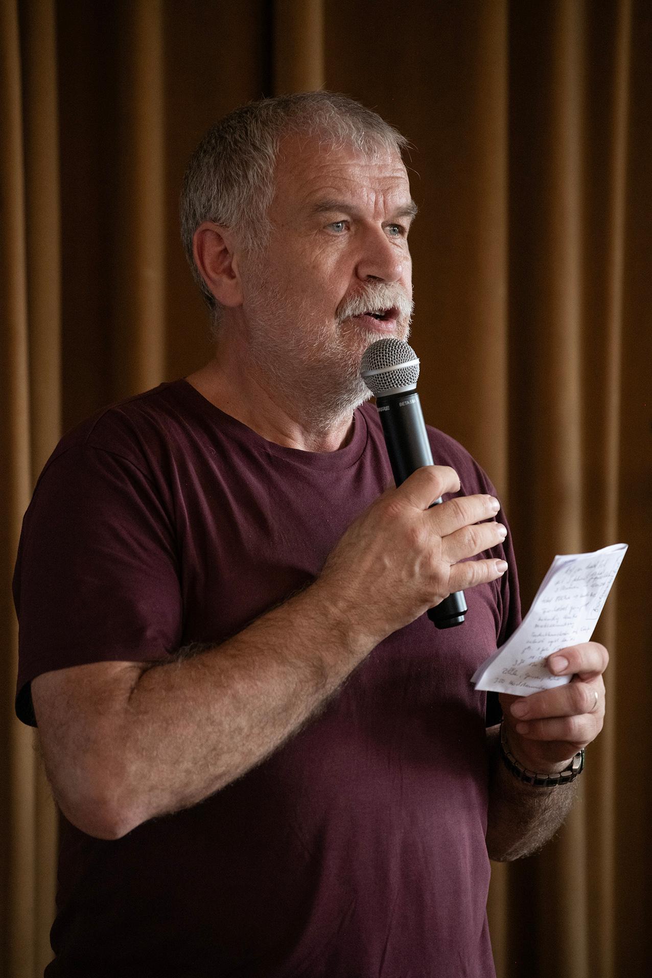 Theo Meier sprechend mit einem Mikrofon und einem Notizzettel in der Hand.