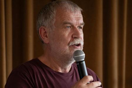 Theo Meier sprechend mit einem Mikrofon und einem Notizzettel in der Hand.