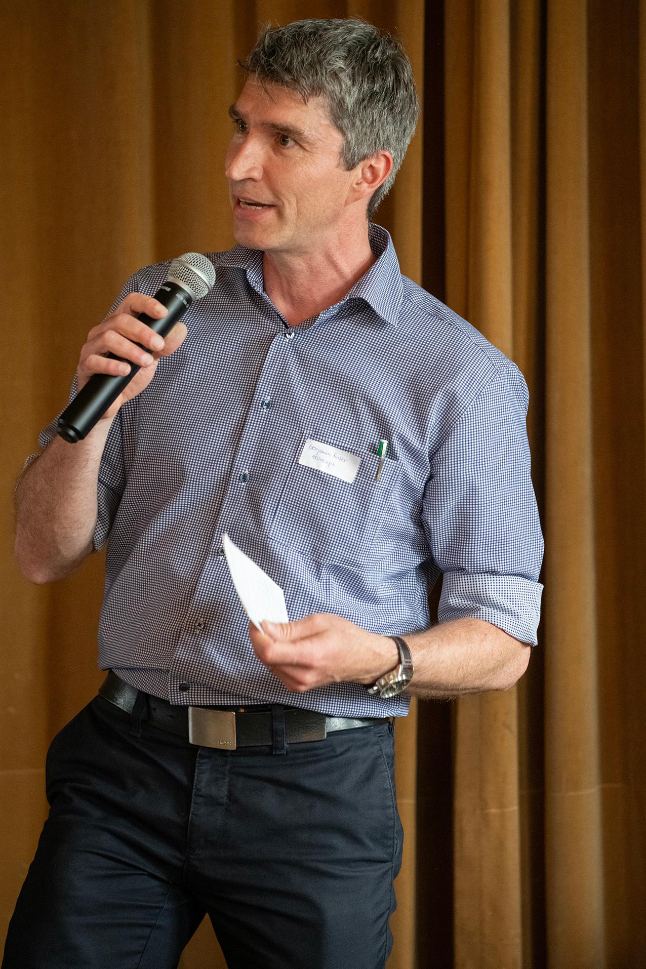 Benjamin Buser sprechend mit einem Mikrofon und Notizen in der Hand.