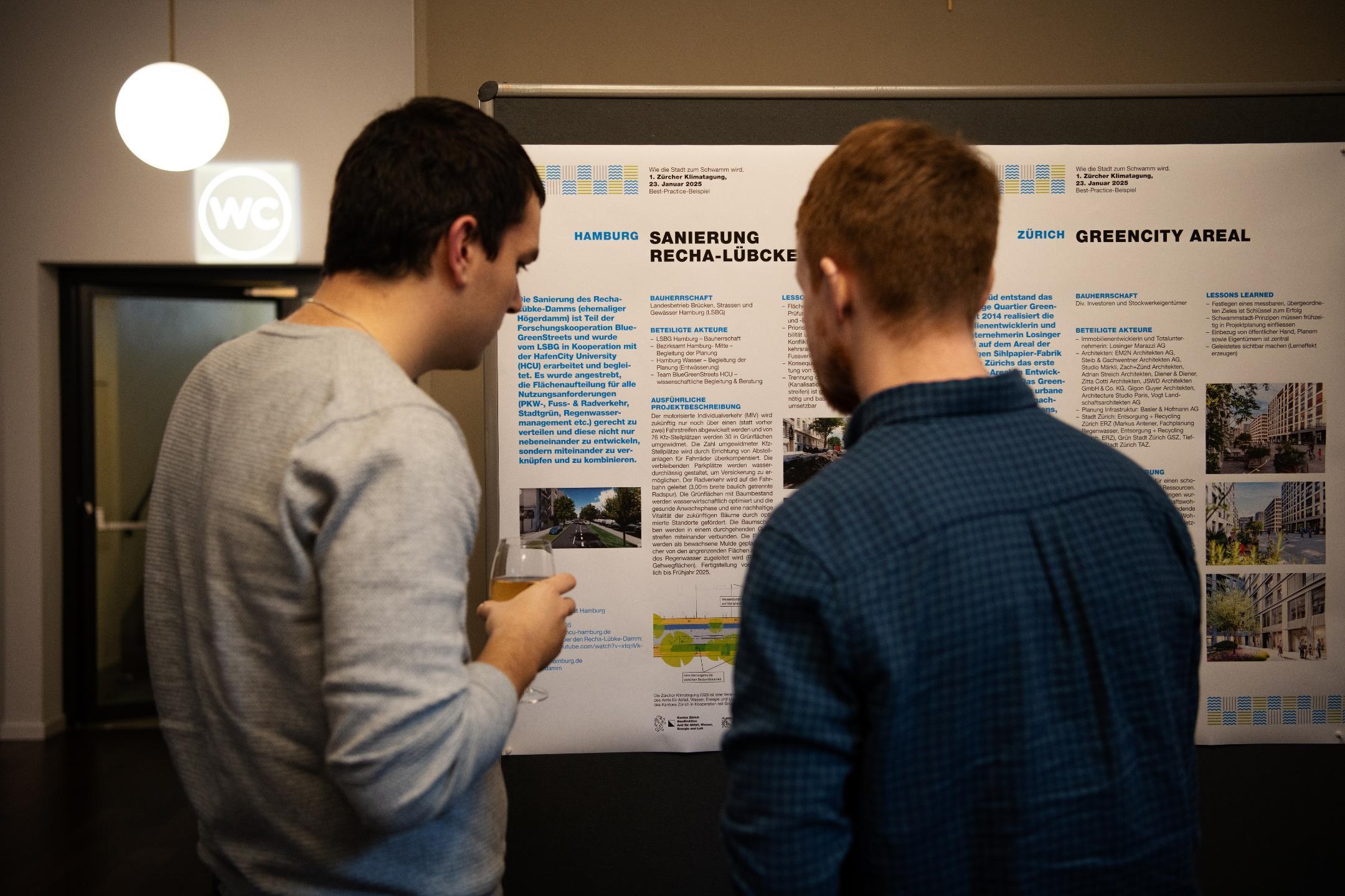 Zwei Teilnehmende der Klimatagung lesen ein Plakat.