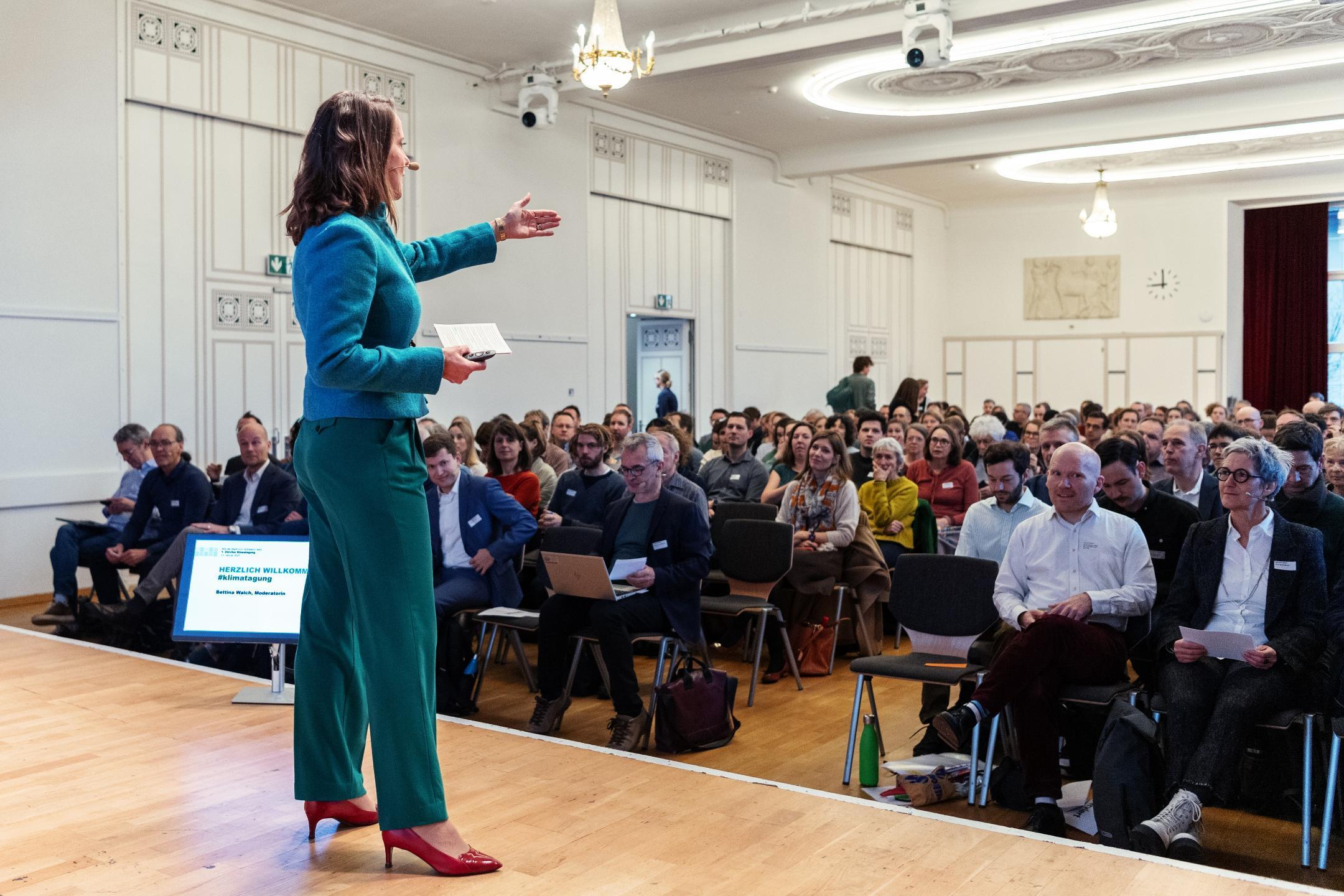 Moderatorin Bettina Walch auf der Bühne vor den Teilnehmenden der Klimatagung.
