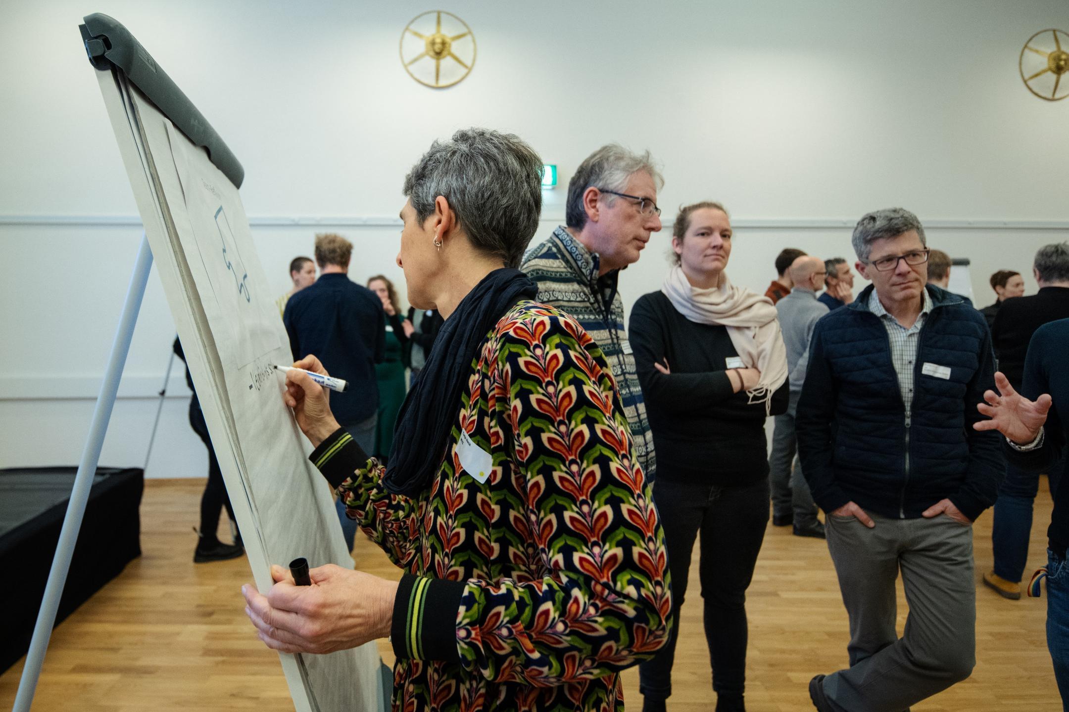 Teilnehmende eines der Workshops an der Klimatagung diskutieren im Hintergrund. Im Vordergrund schreibt eine Teilnehmende etwas auf ein Board.