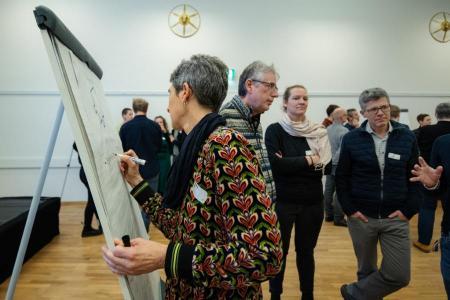 Teilnehmende eines der Workshops an der Klimatagung diskutieren im Hintergrund. Im Vordergrund schreibt eine Teilnehmende etwas auf ein Board.