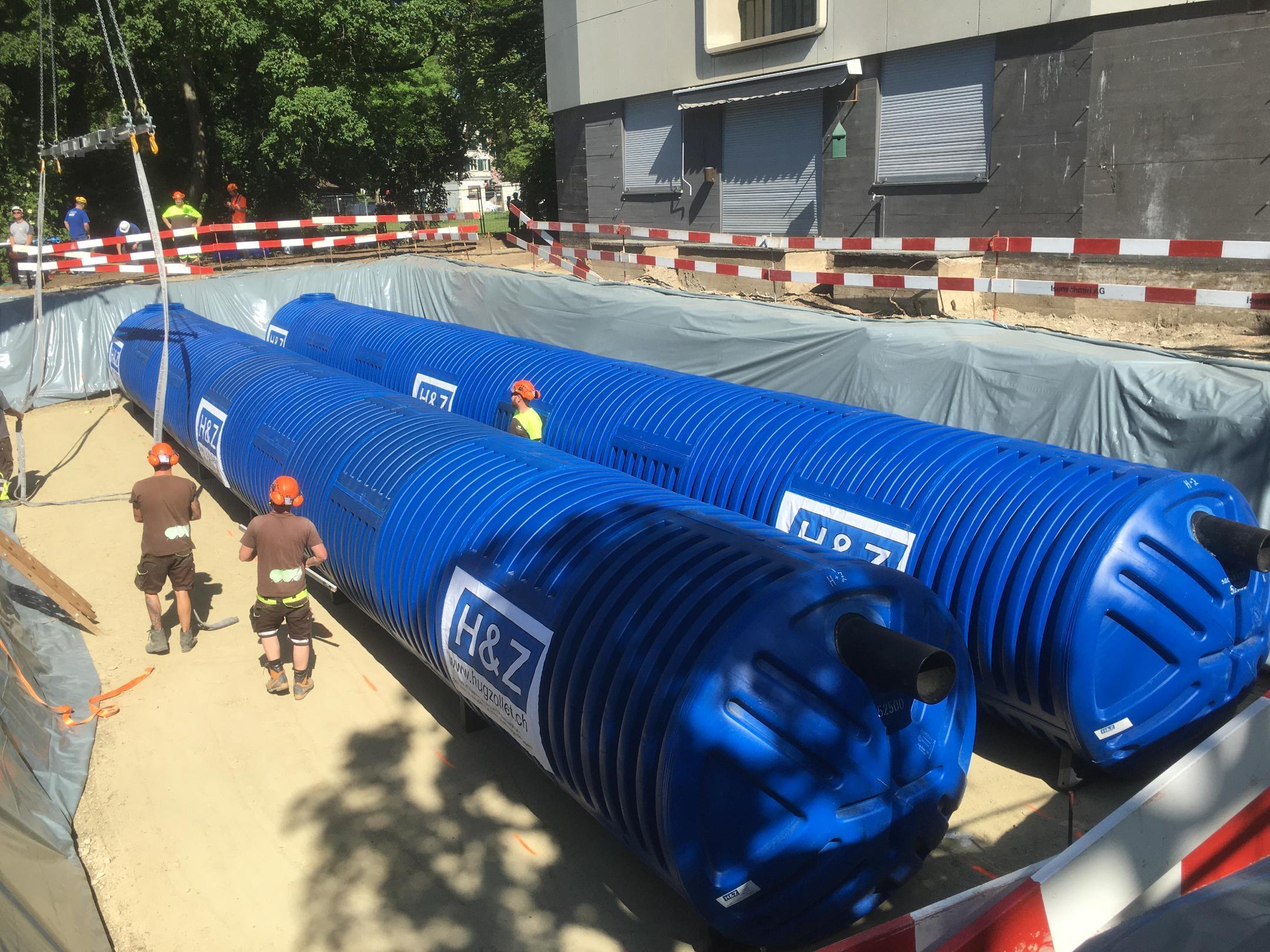 Grosse blaue Regenwasserspeicher-Rohre die in Baugrube durch Bauarbeiter montiert werden.
