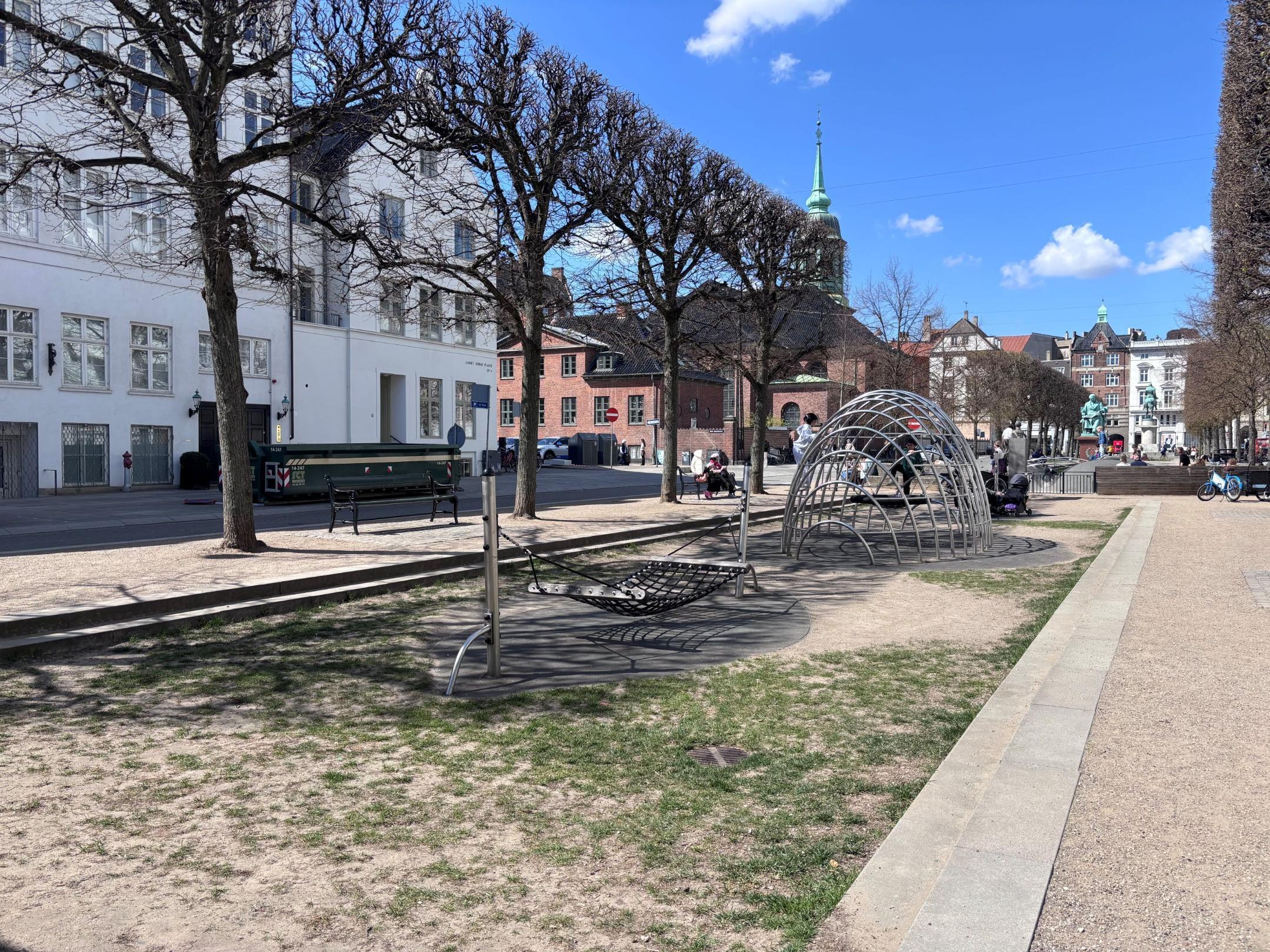 Das Foto zeigt einen Boulevard. In der Mitte hat es einen Kinderspielplatz. Der Kinderspielplatz ist über zwei Treppentritte abgesenkt.