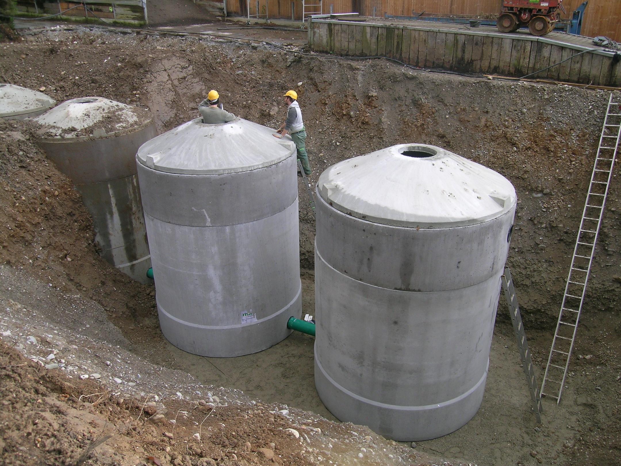 Grosse graue Zisternen die in einer Baugrube durch Bauarbeiter aufgebaut werden.