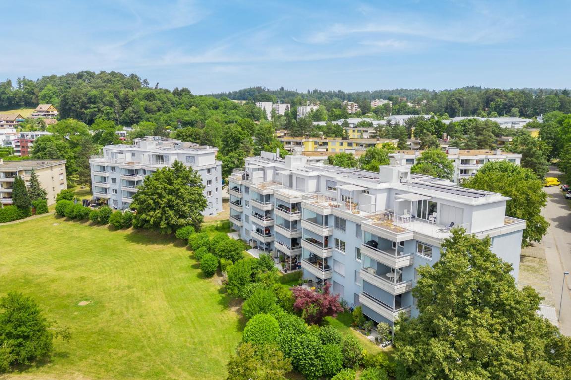 Eine sanierte Überbauung mit drei Mehrfamilienhäusern in Volketswil. Auf den Dächern sind Photovoltaikanlagen, rundherum viel Grün.