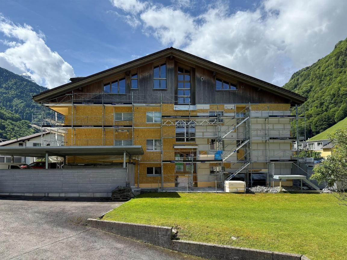 Bei dem eingerüsteten Mehrfamilienhaus sind links herkömmliche Paneele und rechts mit der Fertigbauweise gefertigte Paneele angebracht. 