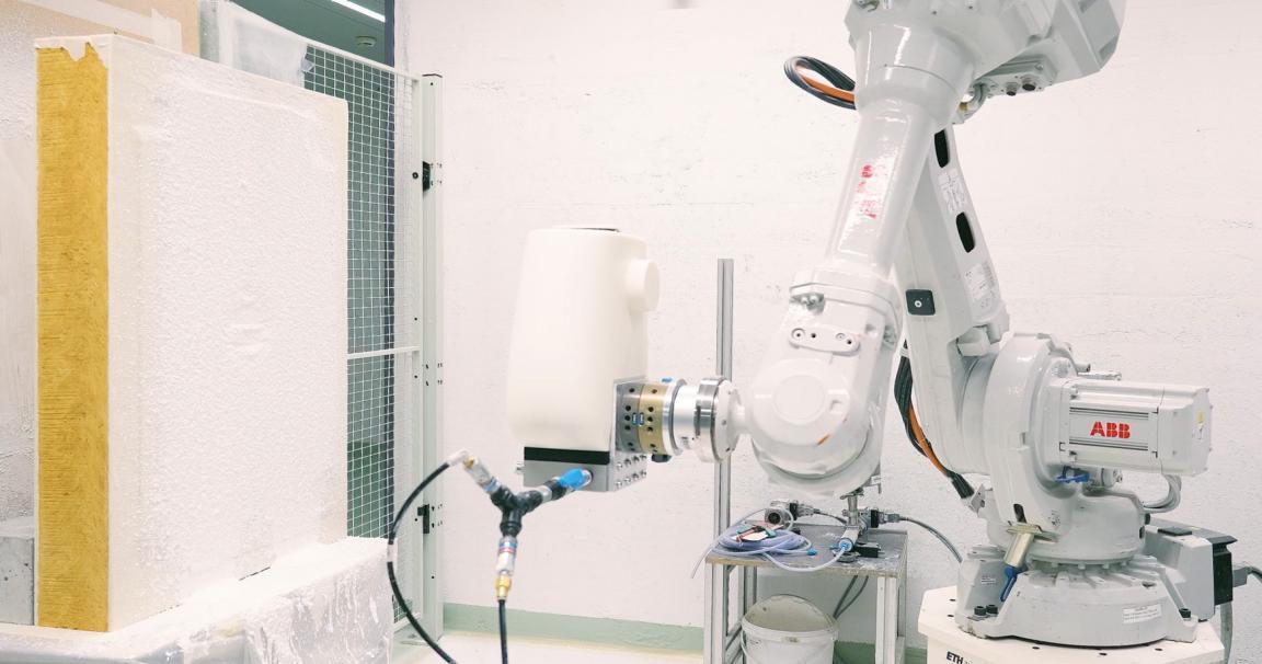 Ein Roboterarm spritzt Material auf die Leichtbauplatte